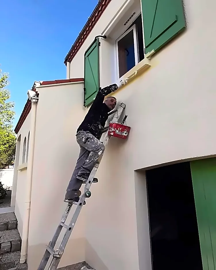 Patrick Halgand, artisan peintre, en train de peindre une façade sur un chantier